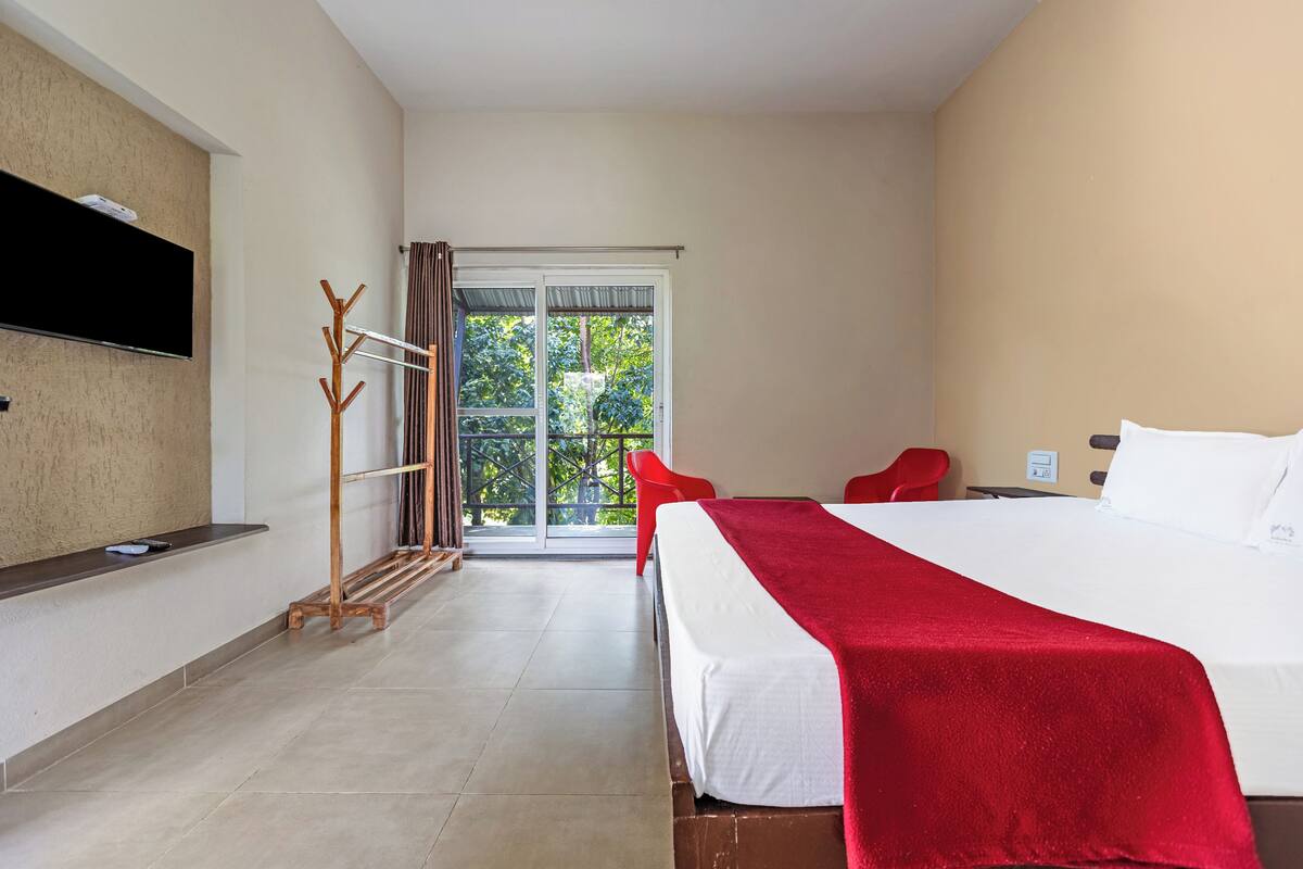 Habitación de hotel con cama, televisión, perchero, una silla y vistas al exterior.