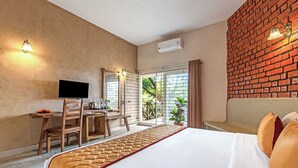 Ein Hotelzimmer mit Bett, Schreibtisch mit Fernseher, Stuhl und Blick ins Grüne durch ein Fenster.
