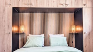 Ein Bett mit Holz-Kopfteil, zwei Nachttischlampen und einer dunklen Wand dahinter.