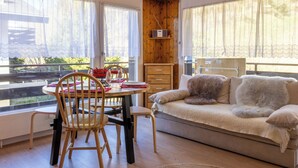 Ein gemütliches Zimmer mit Holzwänden, einer Couch, einem Esstisch mit Stühlen und großen Fenstern.