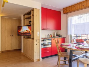 A kitchen with wooden cabinets, a red countertop, and a dining area with a table and chairs. - Ramuges 37A by Interhome (Veysonnaz)