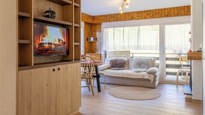 Ein gemütliches Wohnzimmer mit Fernseher, Holzregalen, einer Couch und einem großen Fenster.