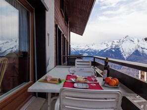 Ein Esstisch mit Blick auf schneebedeckte Berge, eine Weinflasche und ein Teller Essen auf einem Balkon.