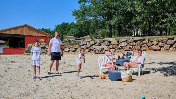 A sandy beach with a stone wall, a red building, and a group of people relaxing on white chairs. - Villa in Pyrenees With Pool and Terrace (Quillan)