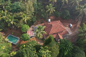 An aerial view of a house with a red-tiled roof, surrounded by dense tropical vegetation and palm trees. - Vayuvana Heritage  (Mananthavady)
