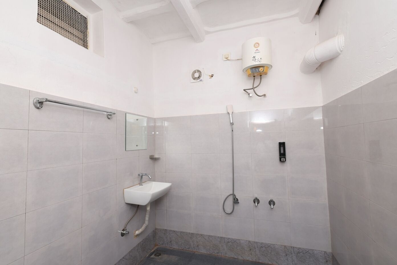 Un baño moderno con ducha a ras de suelo, cabezal de ducha de mano, secador de pelo montado en la pared y un lavamanos pequeño con espejo.