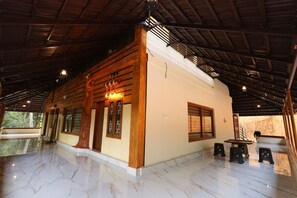 A spacious room with a high ceiling, wooden beams, a marble floor, and a large window. - Vayuvana Heritage  (Mananthavady)