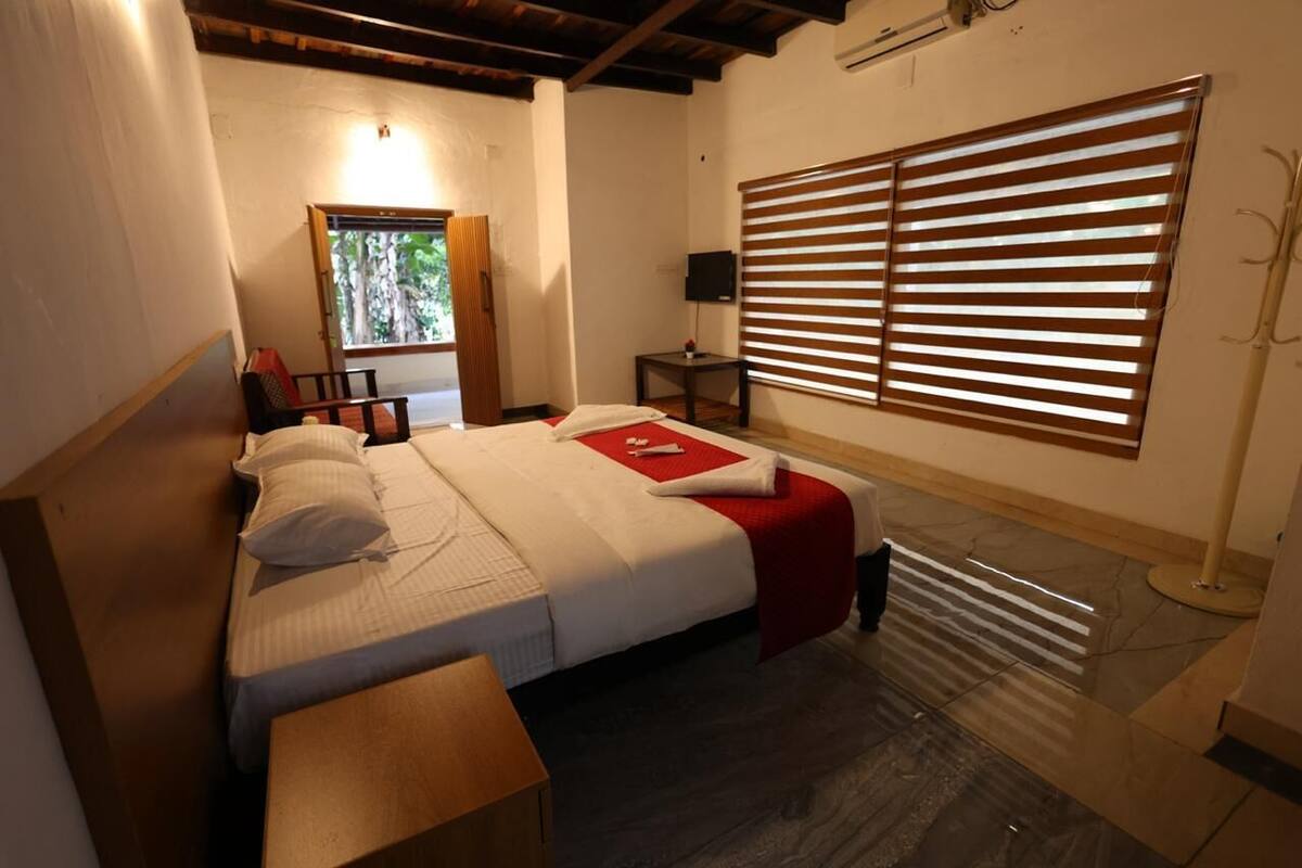 Ein Schlafzimmer mit Bett, Nachttisch, Fenster mit Jalousien und Blick ins Grüne.