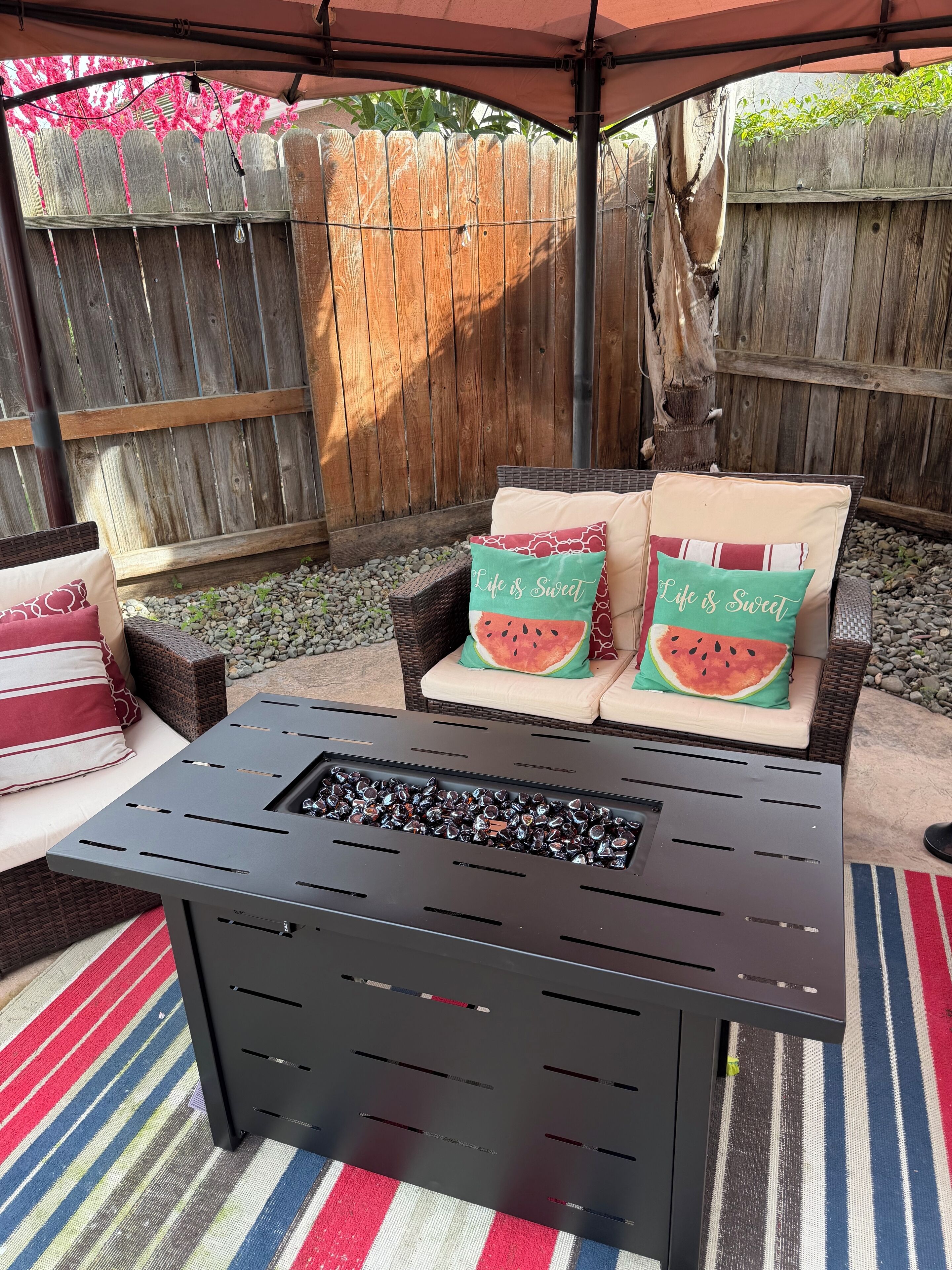 Ein Außenbereich mit Terrasse, einem schwarzen Tisch, Korbstühlen und Kissen mit Wassermelonenmuster.