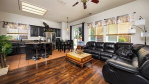 A spacious living area with a leather sofa, wooden coffee table, and a kitchen in the background. - Luxurious 5 Bedroom Retreat with Saltwater Pool (Elk Grove)