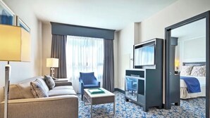 Habitación de hotel con sofá, sillón, televisión y cama con colcha azul.