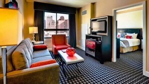 Habitación de hotel con sofá, sillón, televisor y cama con vista a la ciudad.
