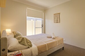 A bedroom with a bed, a nightstand, a lamp, a window with curtains, and a wall hanging. - Walk to Town, Full AC, Golf Course (Dunsborough)
