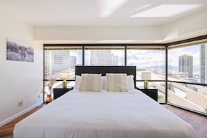 Una habitación de hotel moderna con una cama grande, vistas a la ciudad y una obra de arte enmarcada en la pared.