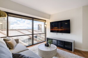 Una sala de estar moderna con un ventanal grande, un televisor de pantalla plana, un sofá, una mesa de centro y una planta.