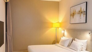 A neatly made bed with white linens, a bedside lamp, and a framed picture on the wall. - Recks Luxury Homes (Abuja)