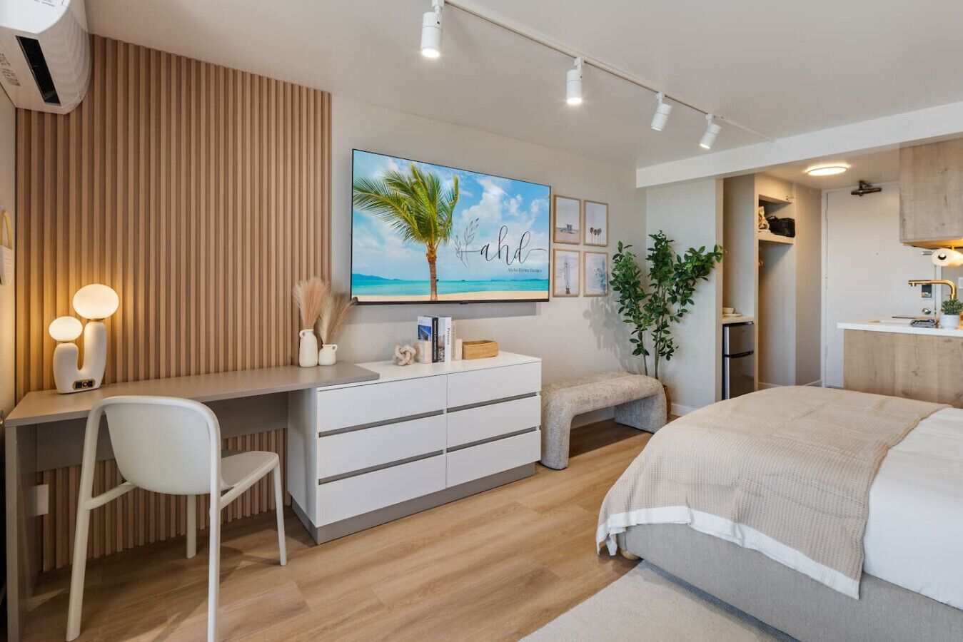 A modern bedroom with a bed, a desk, a chair, a TV, and a plant.