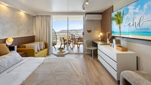 Une chambre d’hôtel moderne dotée d’un grand lit, d’un canapé, d’un bureau et offrant une vue sur la ville grâce à de grandes fenêtres.