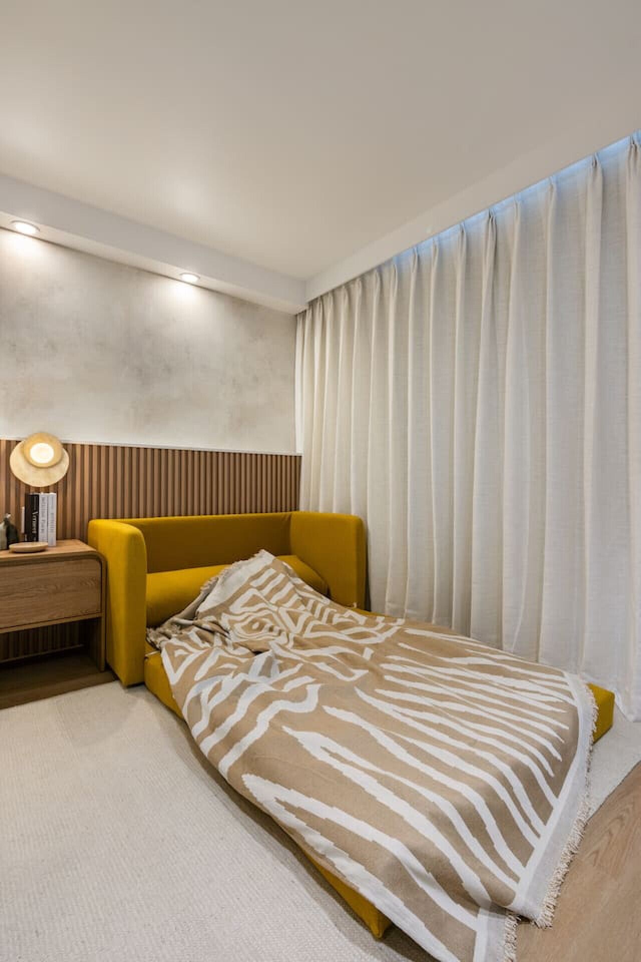 Une chambre moderne avec un lit simple, une table de chevet, une lampe et une fenêtre avec des rideaux.