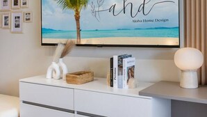Una sala de estar moderna con un televisor de pantalla plana grande montado en la pared, una consola blanca con cajones y un estante decorativo fijado a la pared.
