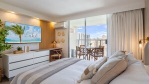 A modern hotel room with a large bed, a desk, and a balcony with a city view. - Oceanview Luxe Retreat – Modern Coastal Elegance (Honolulu)