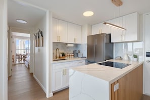 Una cocina moderna con armarios blancos, una isla grande, electrodomésticos de acero inoxidable y vistas a un balcón.