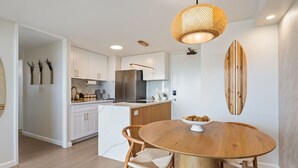 A modern kitchen with white cabinets, a central island, and a round wooden dining table with chairs. - Oceanview Luxe Retreat – Modern Coastal Elegance (Honolulu)