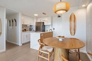 Una cocina moderna con armarios blancos, una isla central y una mesa de comedor redonda de madera con sillas.