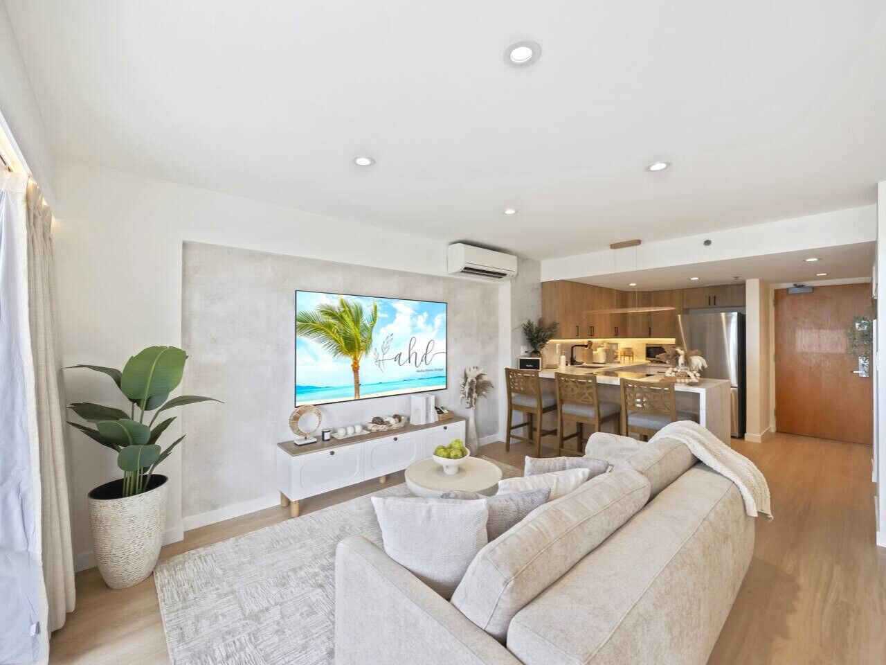 A modern living room with a large flat-screen TV, a sofa, a coffee table, and a dining area with wooden furniture.