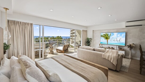 A modern hotel room with a balcony, a sofa, a bed, and a TV. - Waikiki Ocean Wave Escape: Coastal Luxe (Honolulu)