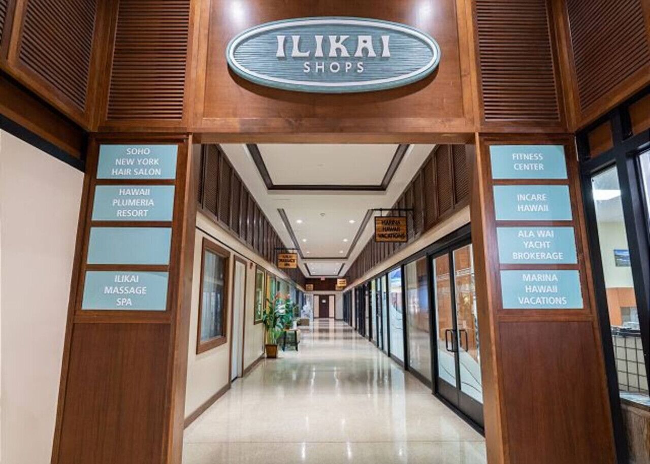 A corridor with signs for ILIKAI MASSAGE SPA, SOHO NEW YORK HAIR SALON, FITNESS CENTER, INCARE HAWAII, ALA WAII YACHT BROKERAGE, and MARINA HAWAII VACATIONS.