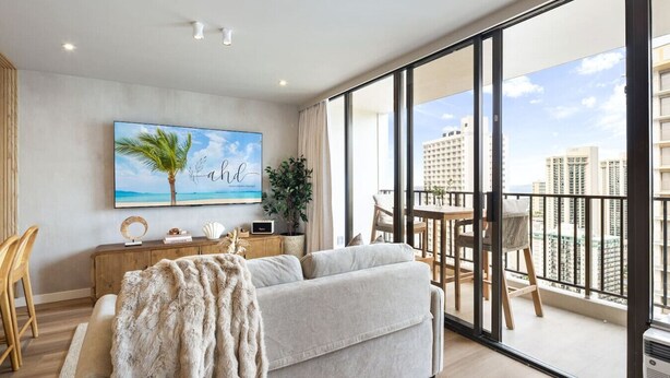 Ein modernes Wohnzimmer mit einem großen Fenster, einem Sofa, einem Couchtisch und einem Gemälde einer Strandansicht.