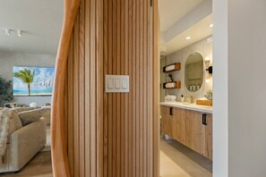 A modern living room with a wooden panel wall, a beige sofa, and a large framed picture of a beach. - Waikiki Luxury Ocean Escape 33F – 1 Parking (Honolulu)