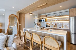 A modern kitchen with a central island, wooden chairs, and a large mirror. - Waikiki Luxury Ocean Escape 33F – 1 Parking (Honolulu)