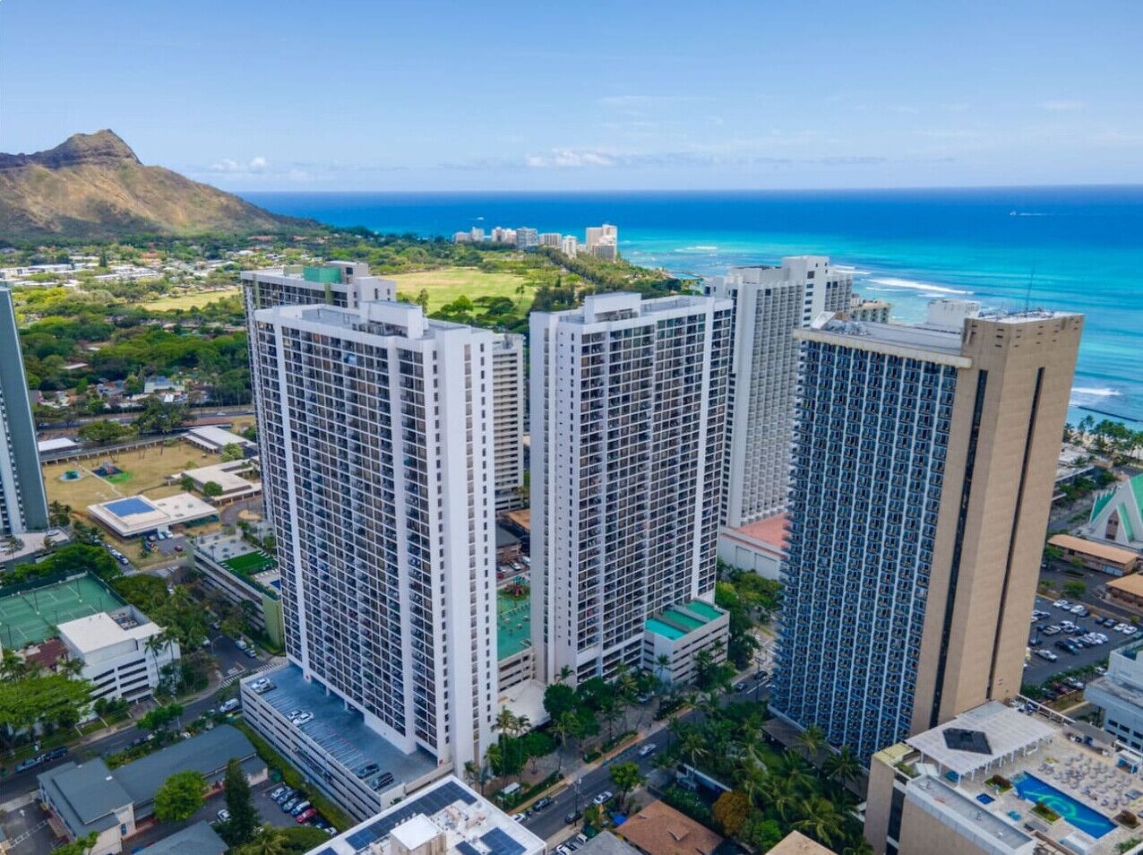 A high-rise building complex with multiple floors, surrounded by greenery and a view of the ocean.