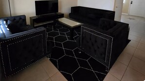 Moderni olohuone, jossa on musta sohva, televisio, kattotuuletin ja kuusikulmio-kuvioinen matto.