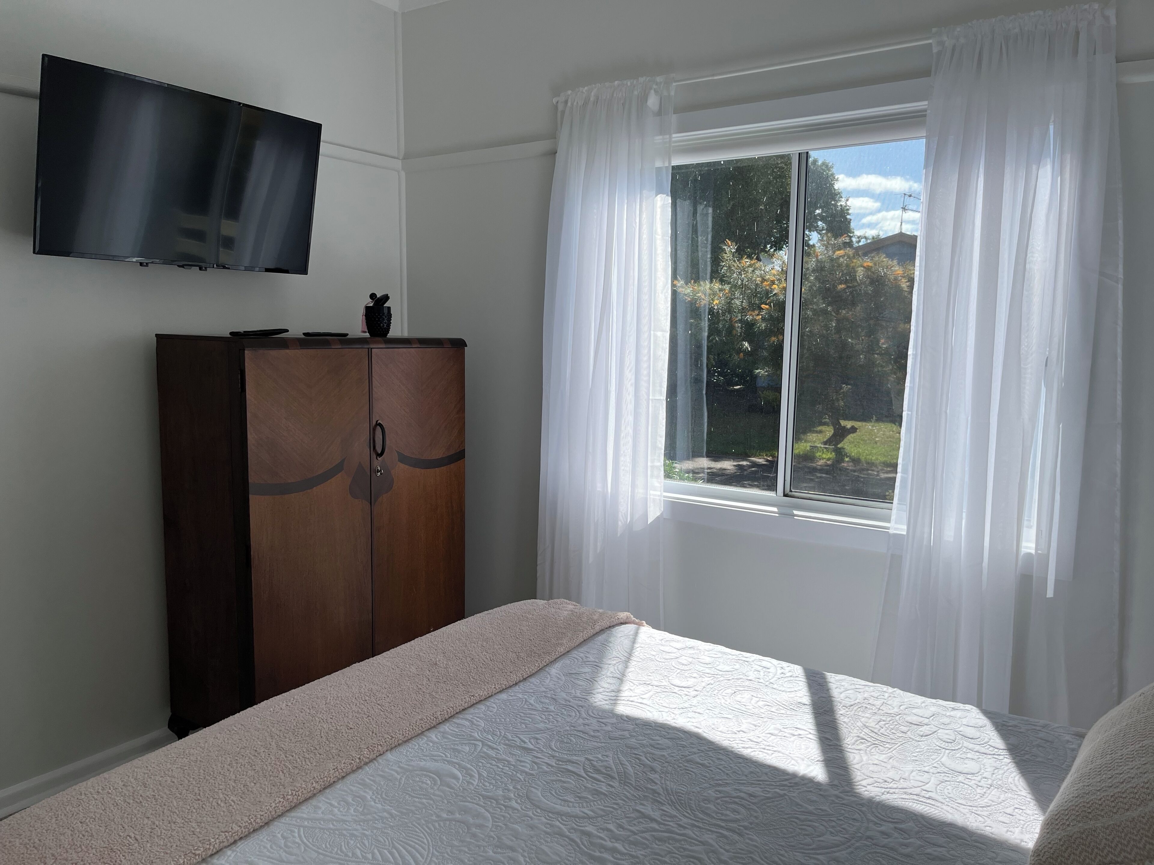 Un dormitori amb llit, un armari, un televisor i una finestra amb cortines.