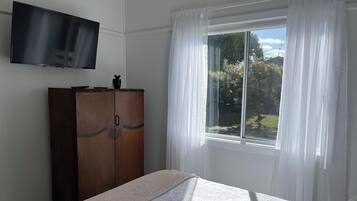 Un dormitori amb llit, un armari, un televisor i una finestra amb cortines.
