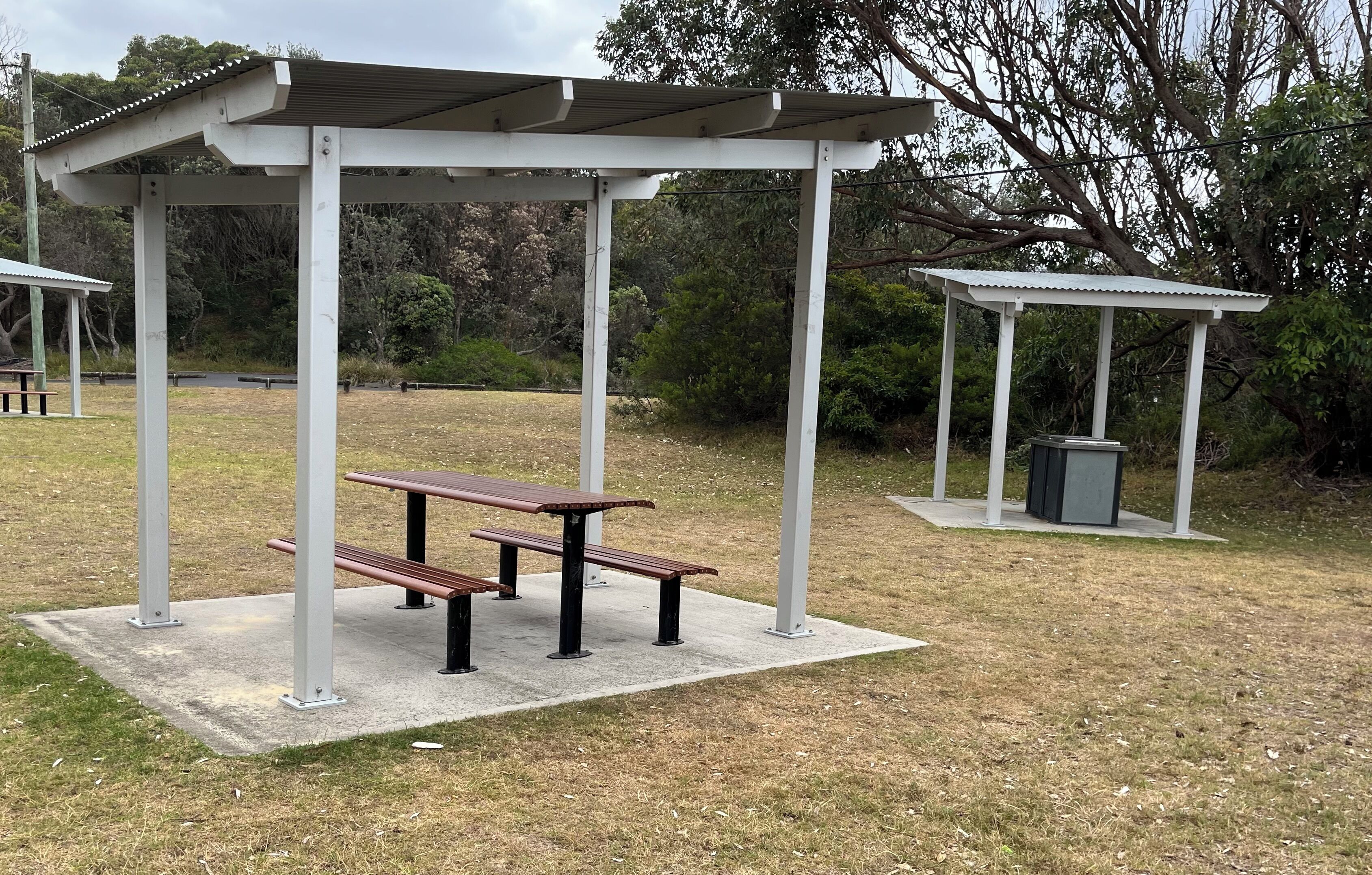 A covered picnic area with benches and a trash bin.