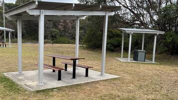 A covered picnic area with benches and a trash bin.