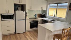 Een moderne keuken met witte kasten, een ingebouwde magnetron, een koelkast, een oven en een spoelbak. Er is een raam met uitzicht en twee houten stoelen zijn zichtbaar.