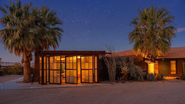 Un edificio moderno con amplias puertas de cristal, palmeras y un paisaje desértico.