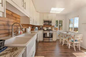 A kitchen with a sink, stove, oven, and a dining area with chairs and a table. - Flutter Space Retreat | Yoga Dome | Pool (Yucca Valley)