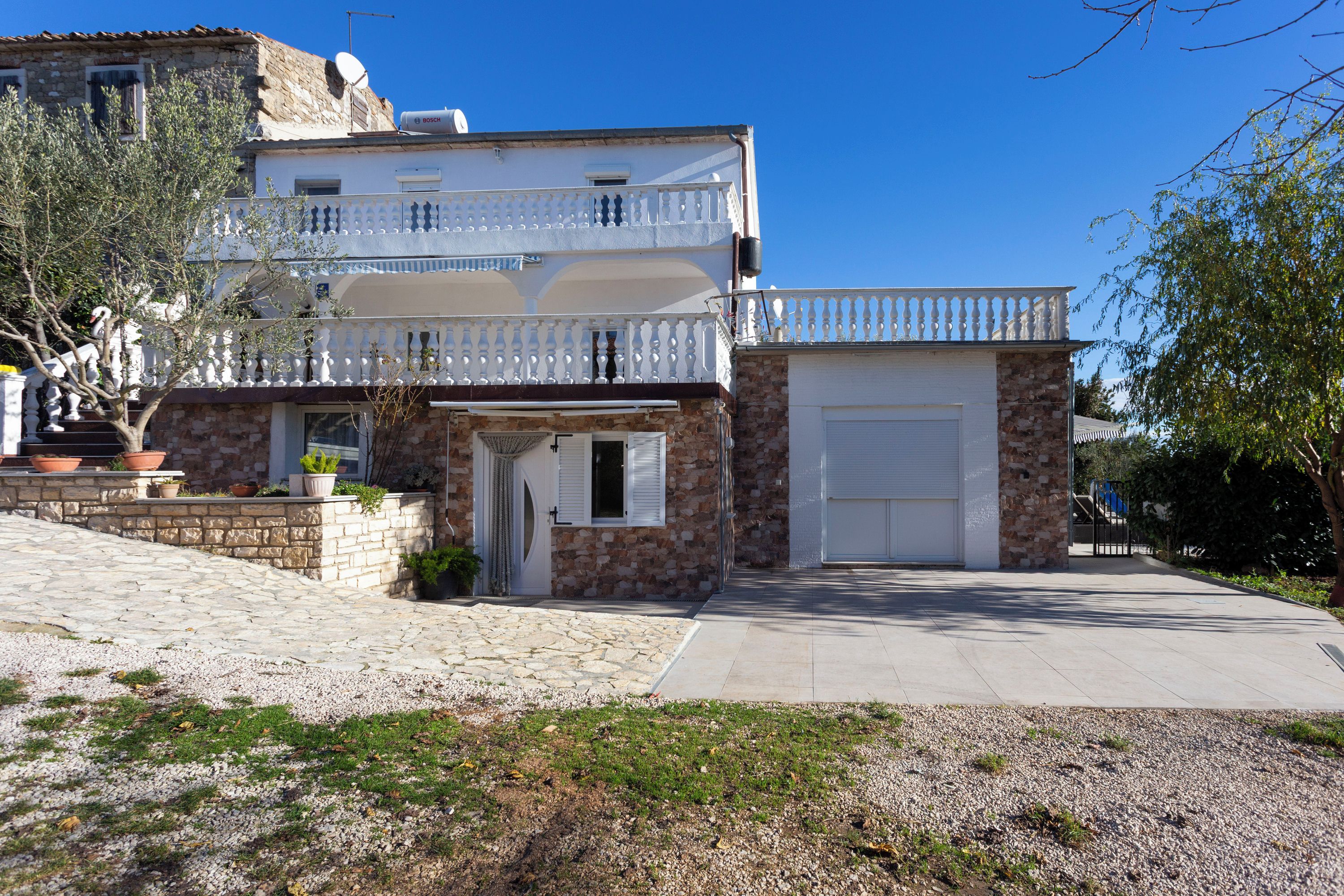 A two-story building with a stone facade, a balcony with white balustrade, and a garage.