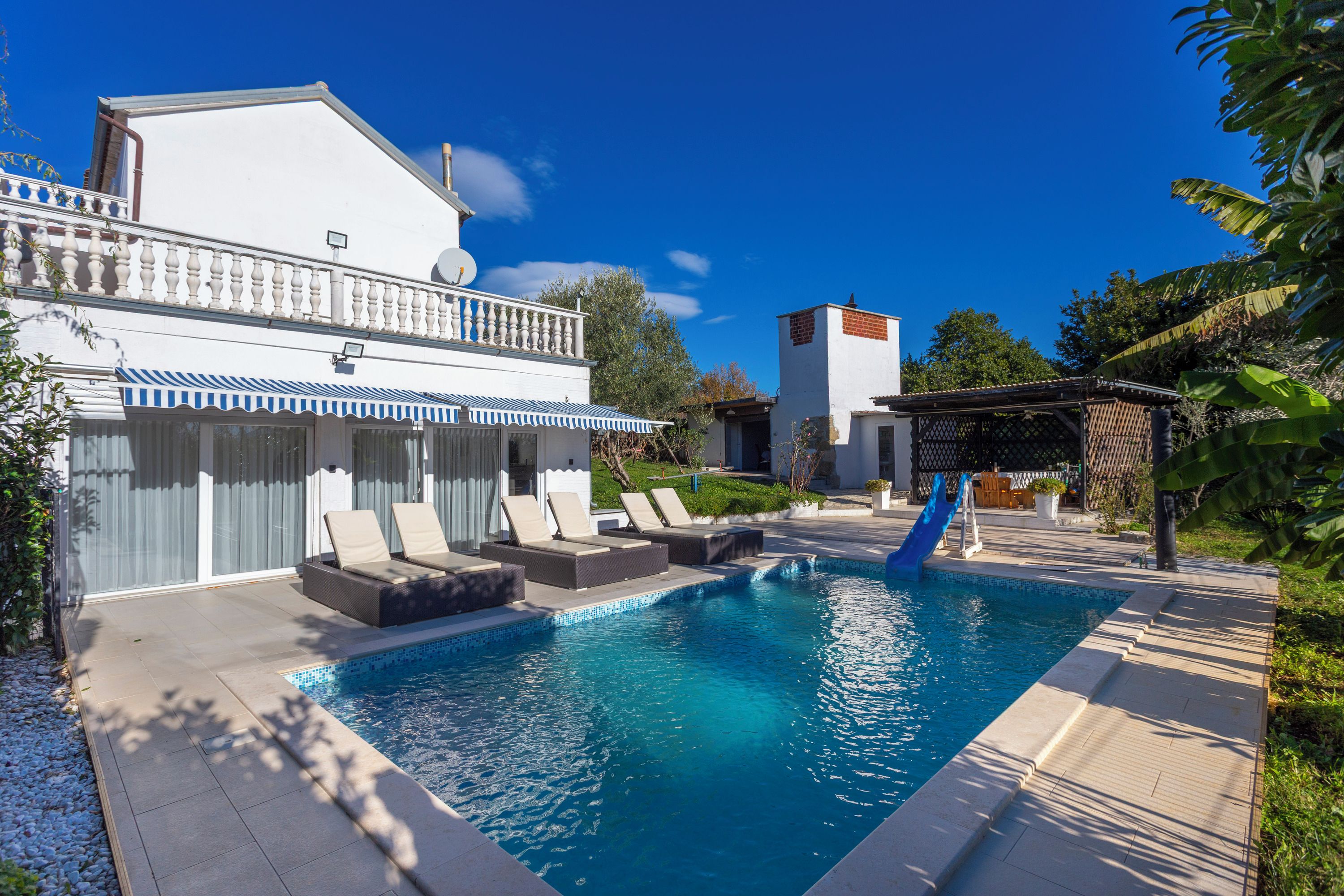 A swimming pool with lounge chairs, a slide, and a building with a balcony.
