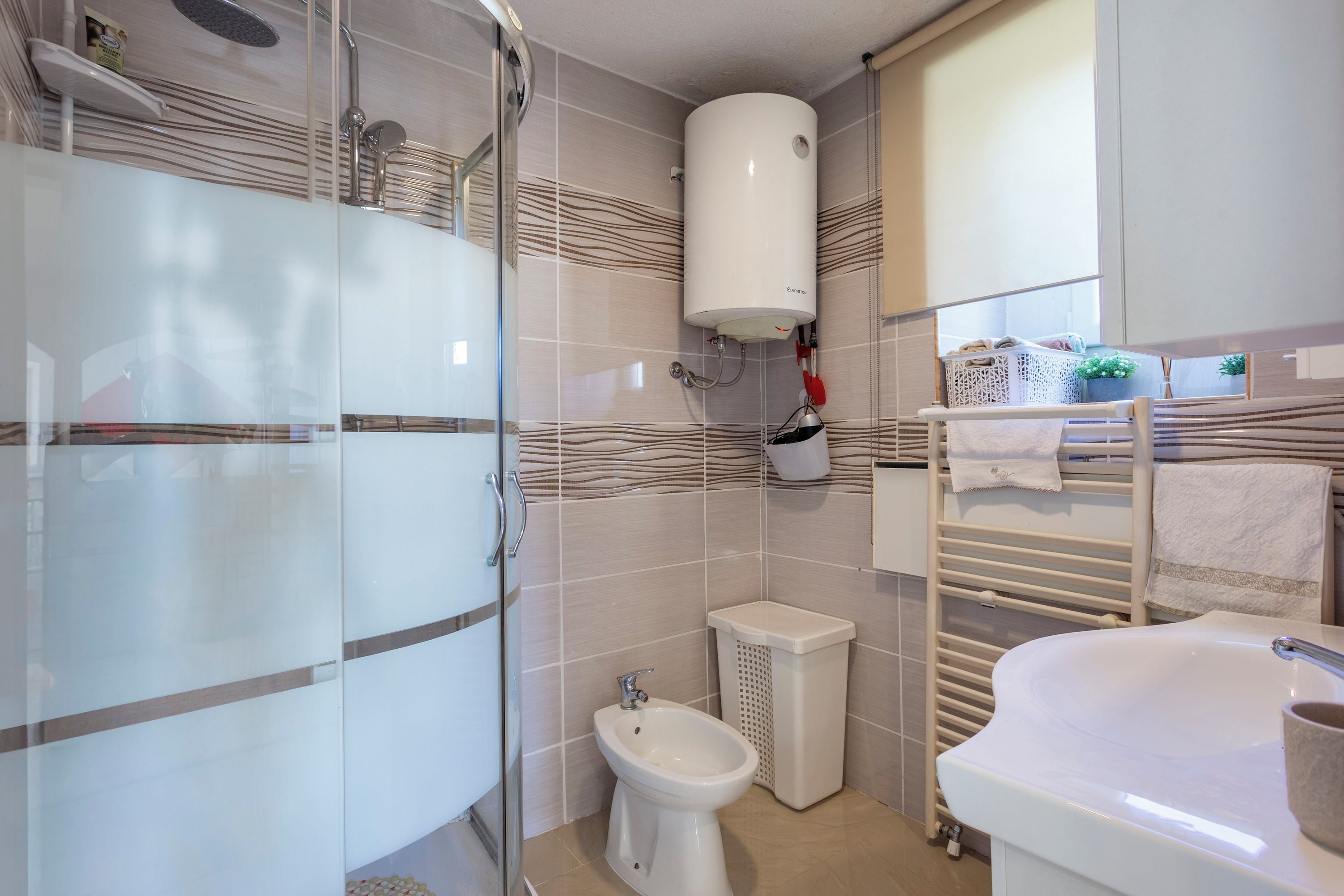 A modern bathroom with a glass shower enclosure, a pedestal sink, a bidet, and a towel rack.