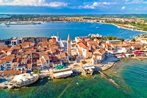 Ilmakuva rannikkokaupungista, jossa on historiallisia rakennuksia, huomattava torni ja venesatama, jossa on useita veneitä.