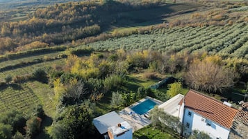 An aerial view of a property with a swimming pool, a white building with a red-tiled roof, and surrounding agricultural fields.