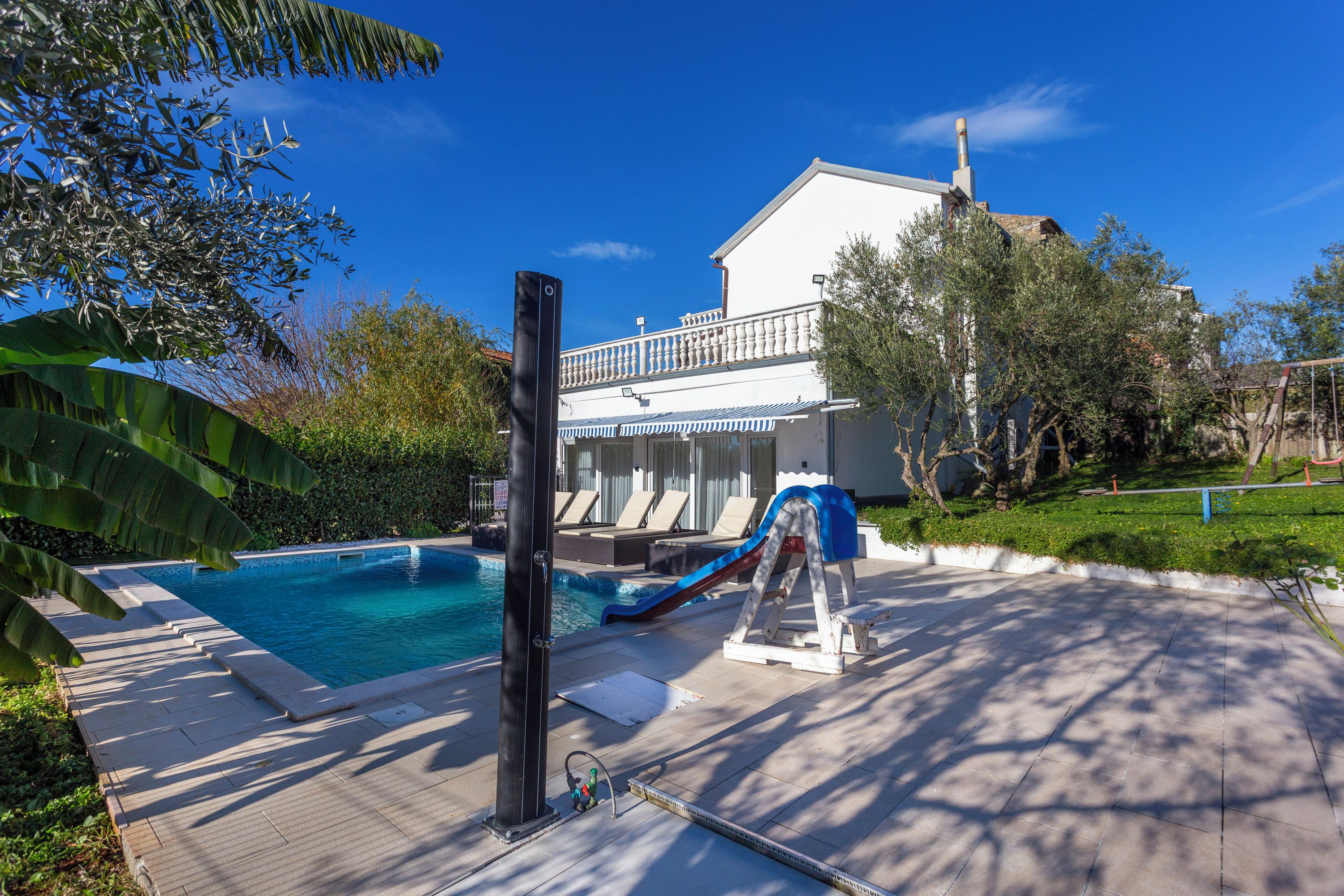 Un espace piscine avec un toboggan, des chaises longues et un bâtiment doté d’un balcon en arrière-plan.