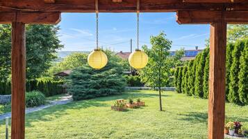 Una pérgola de madera con dos faroles colgantes, rodeada por un jardín cuidado con un camino, plantas en macetas y vistas a una zona residencial.